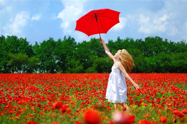 دختر شادی که با چتر قرمز روی مزرعه خشخاش می پرد