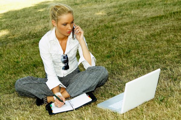 زن تجاری که با کامپیوتر لپ تاپ روی چمن کار می کند
