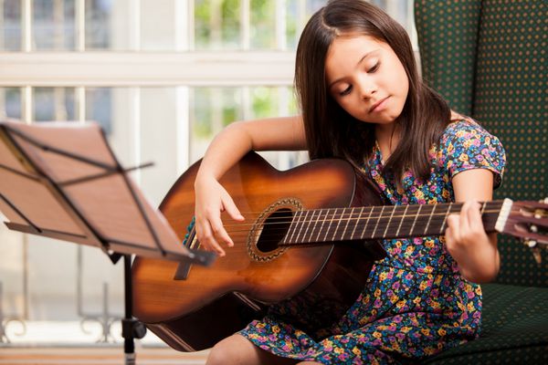 دختر کوچک زیبا در حال تمرین صدای جدید روی گیتار در خانه