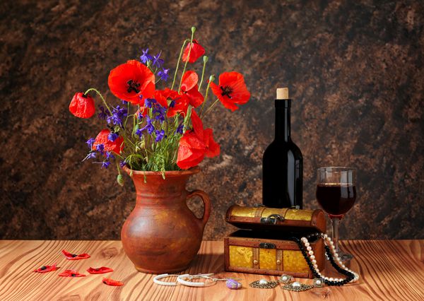 خشخاش قرمز در یک گلدان سرامیکی و جواهرات روی میز