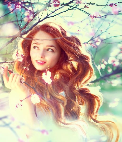 دختر زیبایی بهاری با موهای بلند قرمز در فضای باز درختان شکوفه پرتره زن جوان عاشقانه طبیعت