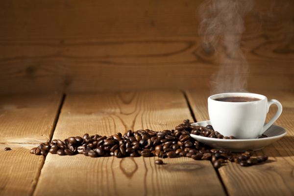 فنجان قهوه سفید و دانه های قهوه در پس زمینه چوبی قدیمی