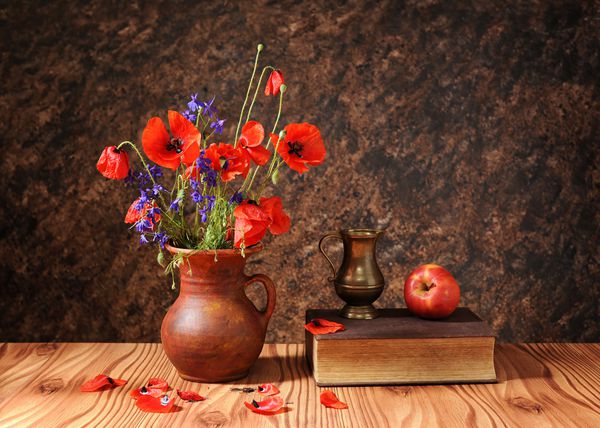 گل خشخاش در یک گلدان با یک سیب روی میز چوبی