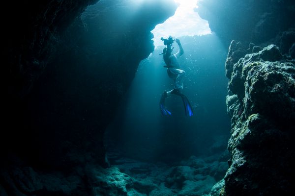 یک غواص آزاد پس از کاوش در غاری در جزیره یاپ میکرونزی به موج سواری صعود می کند صخره های مرجانی در اینجا به مجموعه ای از غارها و شکاف های عمیق فرسایش یافته اند