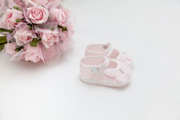 هدیه ای برای نوزاد و مادر گل های صورتی و صندل بچه گانه روی تخت سفید