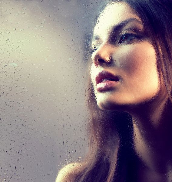 پرتره دختر زیبایی پشت شیشه خیس زن مالیخولیایی باران مدل زیبا که از پنجره با قطره های باران نگاه می کند