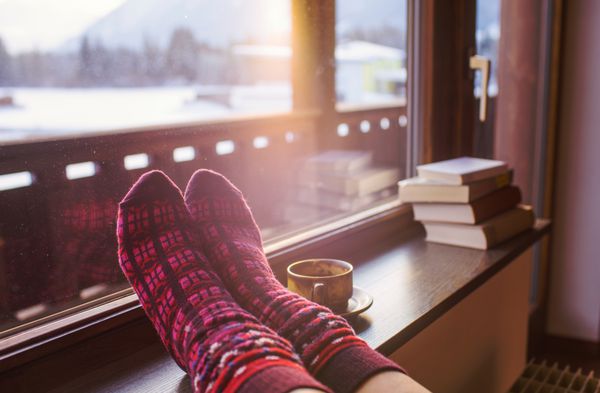 پاها در جوراب های پشمی در کنار چشم انداز کوه های آلپ زن در کنار منظره کوه با یک فنجان نوشیدنی استراحت می کند نزدیک روی پا مفهوم تعطیلات زمستانی و کریسمس