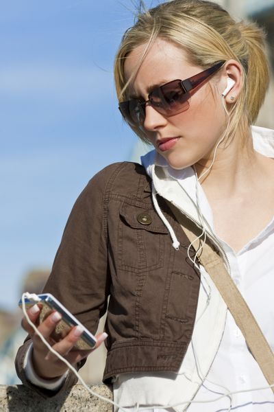 یک زن جوان زیبا در بیرون در حال گوش دادن به موسیقی با پخش کننده mp3 خود