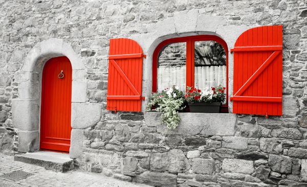 خانه سنگی قدیمی با کرکره های چوبی قرمز و در قرمز جعبه هایی با گل های قرمز و سفید روی پنجره بریتنی فرانسه رترو سن po