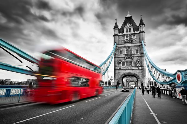 اتوبوس قرمز در حال حرکت بر روی پل برج در لندن انگلستان ابرهای بارانی چشمگیر سیاه و سفید با عناصر پل قرمز و آبی