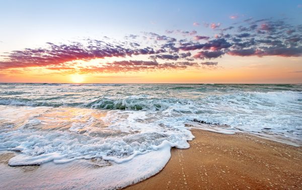 طلوع خورشید رنگارنگ ساحل اقیانوس با آسمان آبی عمیق و پرتوهای خورشید