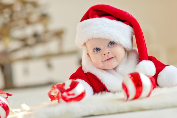 کودک خوشحال لبخند روی شکم دراز کشیده است و کلاه و کت و شلوار بابا نوئل قرمز و سفید را پوشیده است و روی زمینه سفید جدا شده است