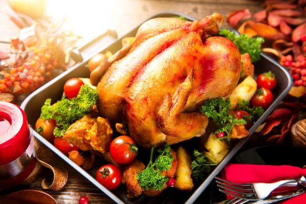 شام مراسم شکرگزاری بوقلمون کبابی که با سیب زمینی سبزیجات و زغال اخته تزئین شده روی میزی به سبک روستایی که با برگ های پاییزی و شمع تزئین شده است شام کریسمس میز سرو میز چیدمان
