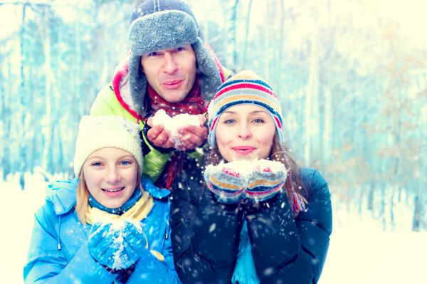 خانواده زمستانی در فضای باز خانواده شاد با بچه در حال دمیدن برف زمستان سرگرمی زمستانی