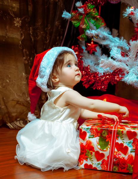 دختر بچه ناز با کلاه بابا نوئل اولین هدیه کریسمس خود را باز می کند سال نو خلق و خوی کریسمس
