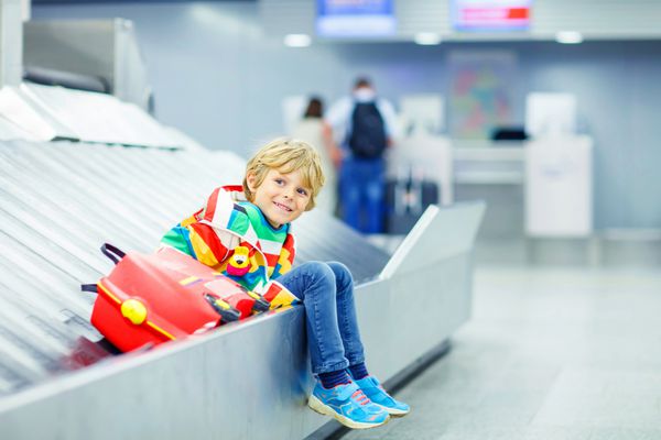 پسر بچه خسته کوچولوی زیبا در فرودگاه در حال مسافرت کودک شاد با چمدان بچه ها روی چرخ فلک چمدان منتظر است لغو پرواز به دلیل اعتصاب خلبان