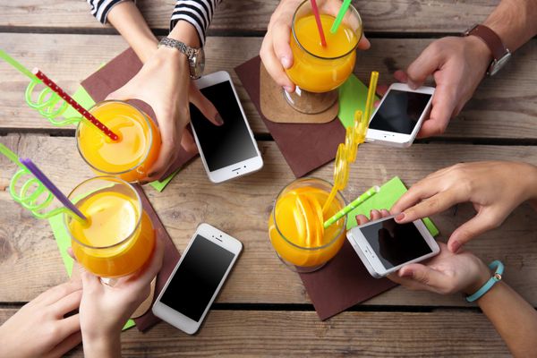 چهار دست با تلفن های هوشمند که دم در دست دارند روی پس زمینه میز چوبی