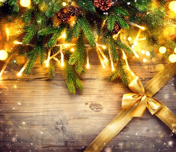 درخت صنوبر کریسمس با تزئین در پس زمینه تخته چوبی تیره طرح هنر حاشیه با درخت کریسمس گلدسته گلدسته روشن و روبان هدیه طلایی با پاپیون