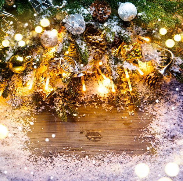 طراحی قاب کریسمس درخت صنوبر با دکوراسیون پرنعمت روی پس زمینه تخته چوبی تیره با برف طراحی هنر مرزی با درخت کریسمس گلدسته‌ها و گلدسته‌های روشن
