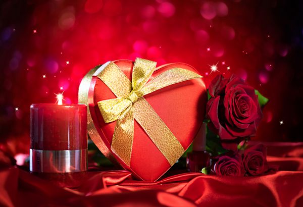 جعبه هدیه قلب قرمز و گل رز قرمز و شمع شعله ور در زمینه ابریشم قرمز روی پس زمینه درخشان تعطیلات خیابان طراحی کارت روز عشق