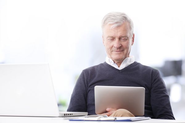 پرتره کلوزآپ تاجر پیر متفکری که روی تبلت دیجیتالی کار می کند در حالی که در دفتر مقابل لپ تاپ نشسته است