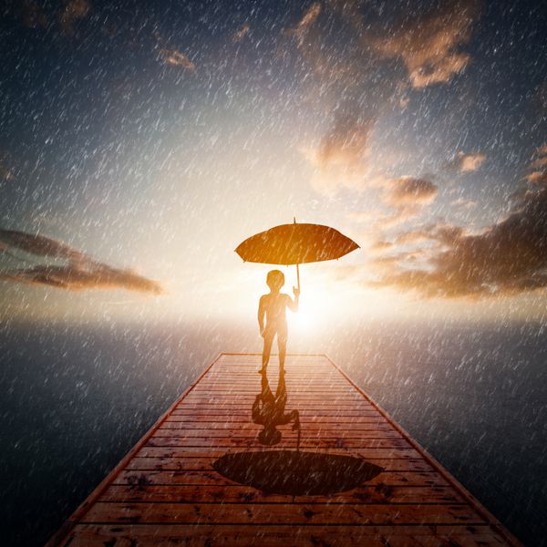 کودکی با چتر که به تنهایی در اسکله چوبی زیر باران ایستاده و به دریا نگاه می کند مفهوم گم شدن تنهایی در یک دنیای بزرگ یا کاوش