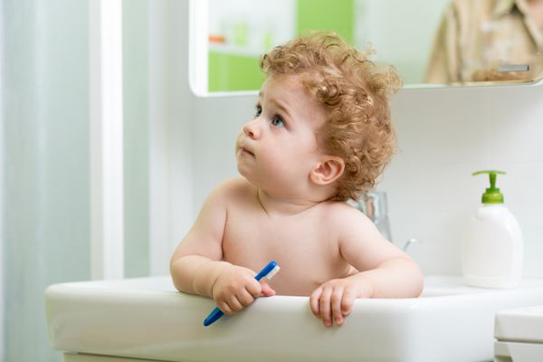 کودک کوچک با مسواک در داخل سینک در حمام نشسته است