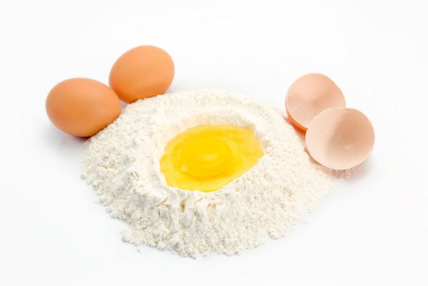 یک تخم مرغ در مقداری آرد آماده برای پخت با تخم مرغ و پوسته تخم مرغ در طرفین