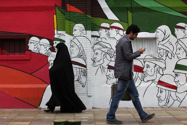 تهران ایران - 3 آوریل 2012 مردم در حال قدم زدن در خیابان امام خمینی با دیوار هنر خیابانی در پس زمینه در مرکز تهران ایران