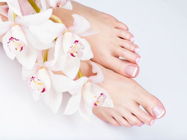 نمای نزدیک از پاهای زن با پدیکور فرانسوی سفید روی ناخن در سالن اسپا مفهوم مراقبت از پاها