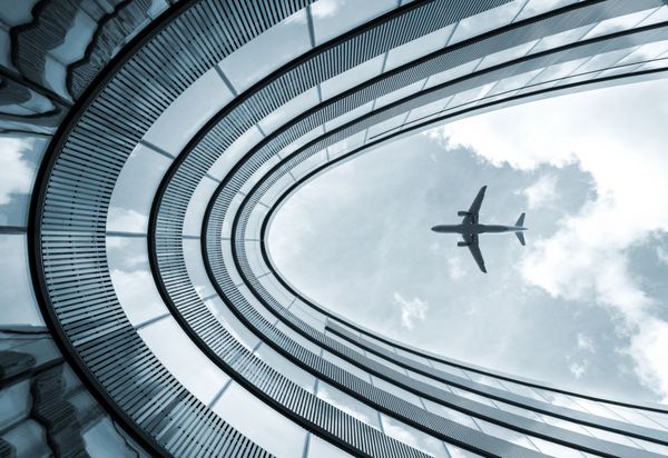 عکس رنگی آبی با نمای کم از ساختمان معماری مدرن با هواپیمای فرود در پس زمینه