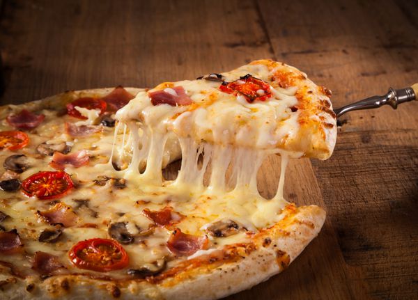 برش پیتزا داغ با ذوب پنیر روی یک میز چوبی روستایی