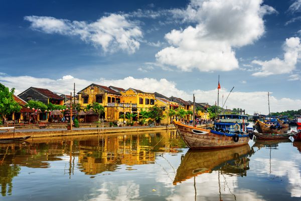 قایق های چوبی بر روی رودخانه thu bon در شهر باستانی هوی hoian ویتنام خانه های قدیمی زرد رنگ در اسکله که در رودخانه منعکس شده است هوی آن یک مقصد گردشگری محبوب در آسیا است