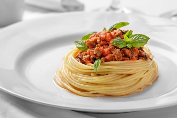 پرتره نزدیک از اسپاگتی ایتالیایی با سس بولونیز روی یک بشقاب سفید ساده