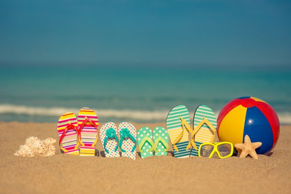 فلیپ فلاپ در ساحل شنی در برابر پس زمینه آبی دریا و آسمان مفهوم تعطیلات تابستانی