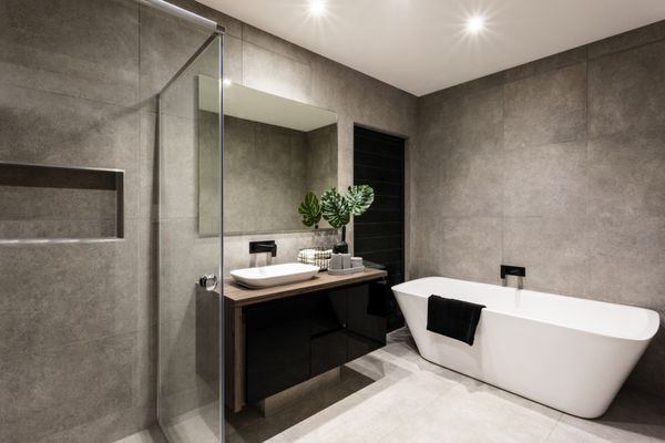 حمام مدرن با فضای دوش و وان حمام شامل یک آینه دیواری در کنار یک گیاه شیک در نزدیکی یک شیر آب و سینک روی پیشخوان چوبی و کمد تاریک