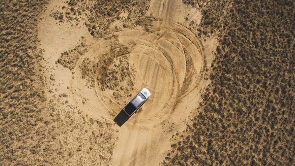 نمای بالای هوایی از پهپاد یک دستگاه پیکاپ سواری در استپ شنی در سفر شگفت انگیز به آسیا سوارکار حرفه ای در حال دریفت کردن در بیابان خشک و بیابانی در حالی که رد لاستیک ها را ترک می کند