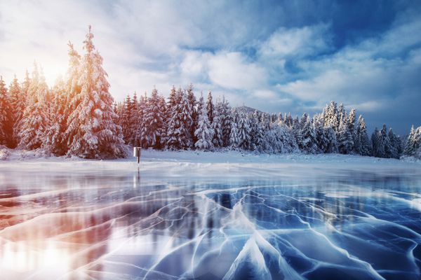 ترک خوردگی روی سطح یخ آبی دریاچه یخ زده در کوه های زمستانی برف می بارد تپه های کاج کارپات اوکراین اروپا