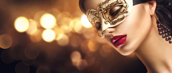 زن مدل زیبایی که ماسک کارناوال بالماسکه ونیزی را در مهمانی روی پس زمینه تیره تعطیلات با درخشش جادویی پوشیده است جشن کریسمس و سال نو خانمی جذاب با آرایش و مدل موی عالی