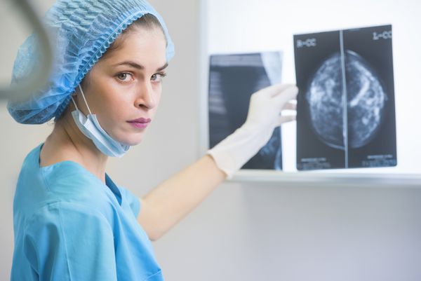زن پزشک یا پرستار با لباس جراحی در حال گرفتن ماموگرافی در مقابل نورپرداز اشعه ایکس است