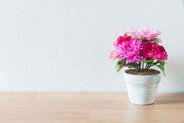 گلدان گل مصنوعی روی میز چوبی و پس زمینه دیوار سفید
