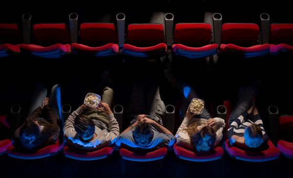 جوانانی که در سینما نشسته اند فیلم تماشا می کنند و پاپ کورن می خورند نمای بالا