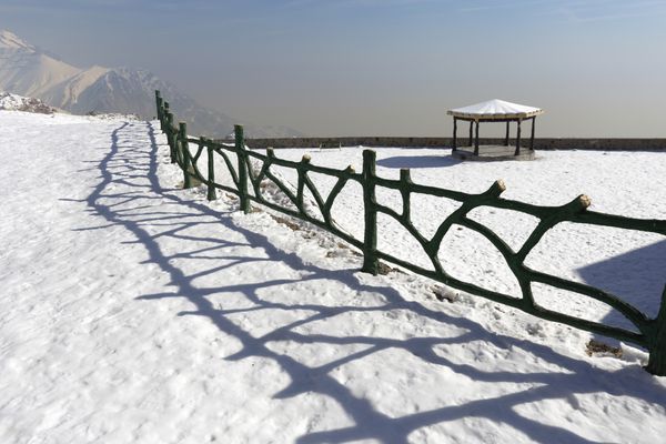 نمای پانوراما کوه توچال در ایستگاه پنجم با حصار چوبی و سایه آن بر روی زمین پوشیده از برف تهران ایران