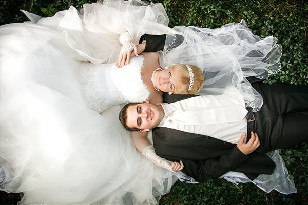 عروس و داماد روی یک چمن سبز دراز کشیده اند