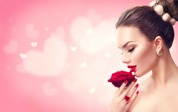 زن روز زیبایی با گل رز قرمز مدل مد دختر پرتره پروفایل با گل رز قرمز در دست لب و ناخن قرمز پس زمینه صورتی تار آرایش و مانیکور زیبای لوکس مو