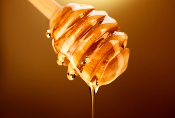 چکیدن عسل از دیپر عسل در زمینه زرد غوطه ور شدن عسل غلیظ از قاشق عسل چوبی مفهوم غذای سالم رژیم غذایی رژیم غذایی