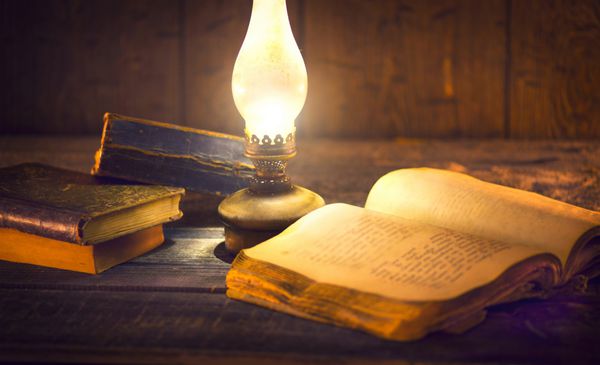 چراغ نفتی قدیمی و کتابهای قدیمی در تاریکی فانوس نفت سفید قدیمی و کتاب باز قدیمی با صفحات خالی روی میز چوبی