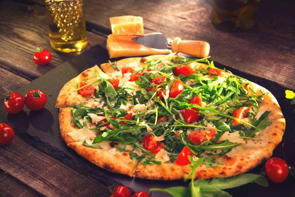 پیتزا کاپریس با آرگولا پنیر ماست و گوجه گیلاسی از نزدیک پیتزای گیاهی خوشمزه خانگی روی میز چوبی غذا
