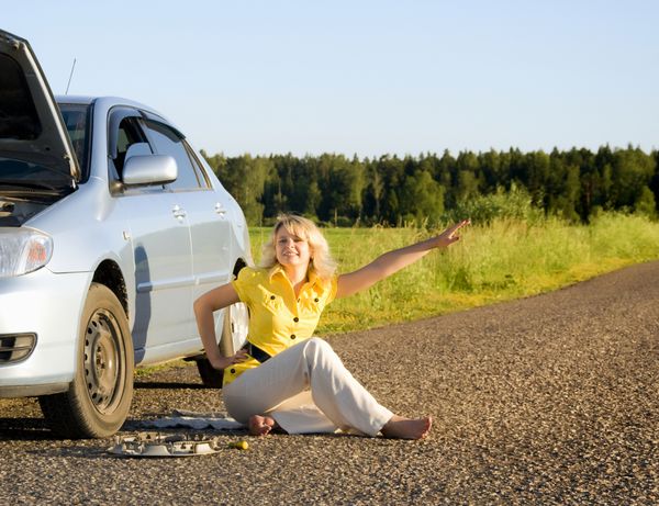دختری در کنار جاده نشسته و کاپوت ماشینش باز است و مشکل ماشین را نشان می دهد