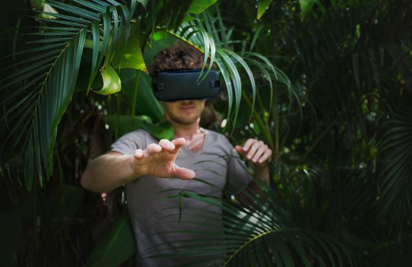 مردی با تی شرت خاکستری هدست واقعیت مجازی سه بعدی و کاوش در نمایشنامه در پس زمینه جنگل طبیعت